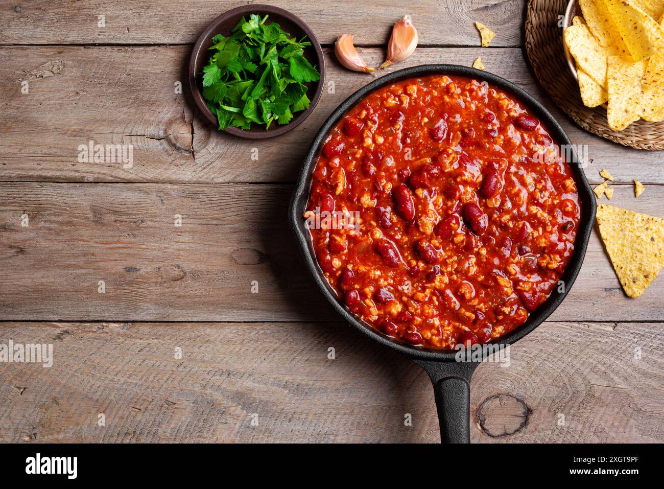 Chili con carne in vaschetta in ghisa con nachos su sfondo in legno, vista dall'alto, spazio per copiare. Cucina messicana. Zuppa piccante con fagioli rossi, peperoni, tom Foto Stock