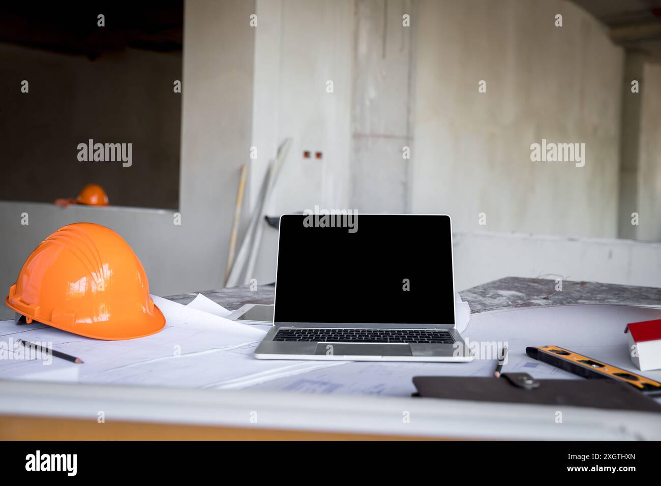 Computer portatile con casco, progetto e modello di casa degli architetti sulla scrivania in cantiere. Foto Stock