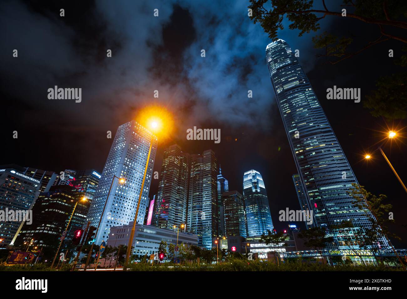 Hong Kong - 19 luglio 2017: Vista notturna della città con grattacieli sotto il cielo nuvoloso scuro, alti edifici per uffici del quartiere centrale Foto Stock