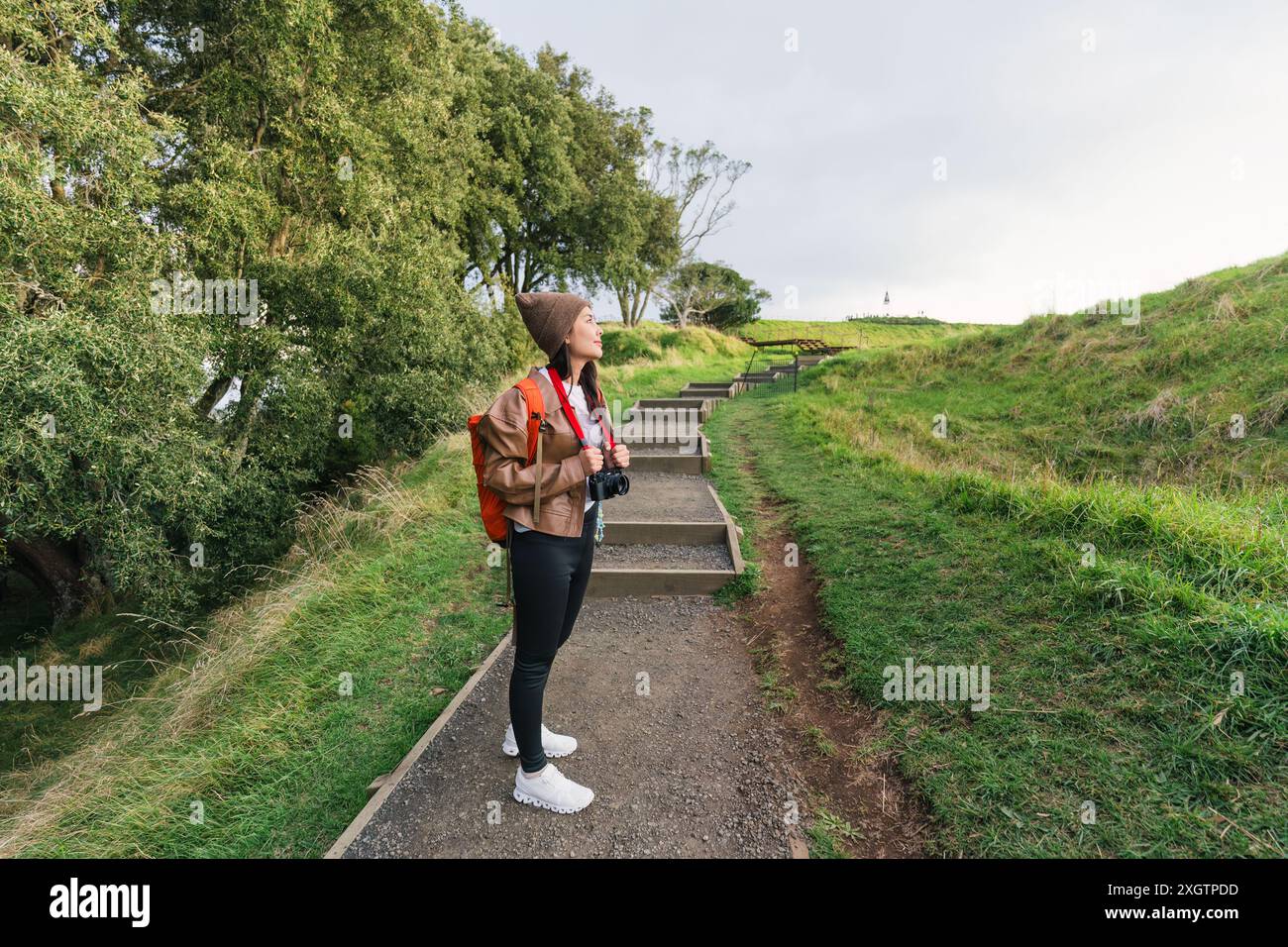 Donna asiatica felice che indossa un berretto che porta con sé una macchina fotografica retrò che fa trekking sulla collina del parco nazionale di Mount Eden, Auckland, nuova Zelanda Foto Stock