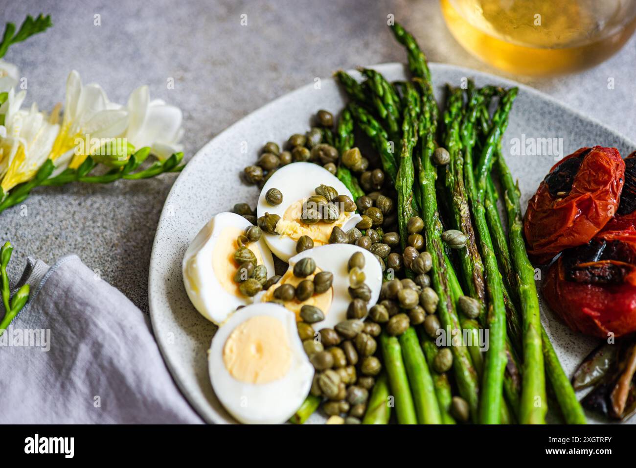 Un pasto nutriente con uova sode, asparagi alla griglia, capperi e verdure grigliate, tra cui pomodori e peperoncino, preparati artisticamente Foto Stock