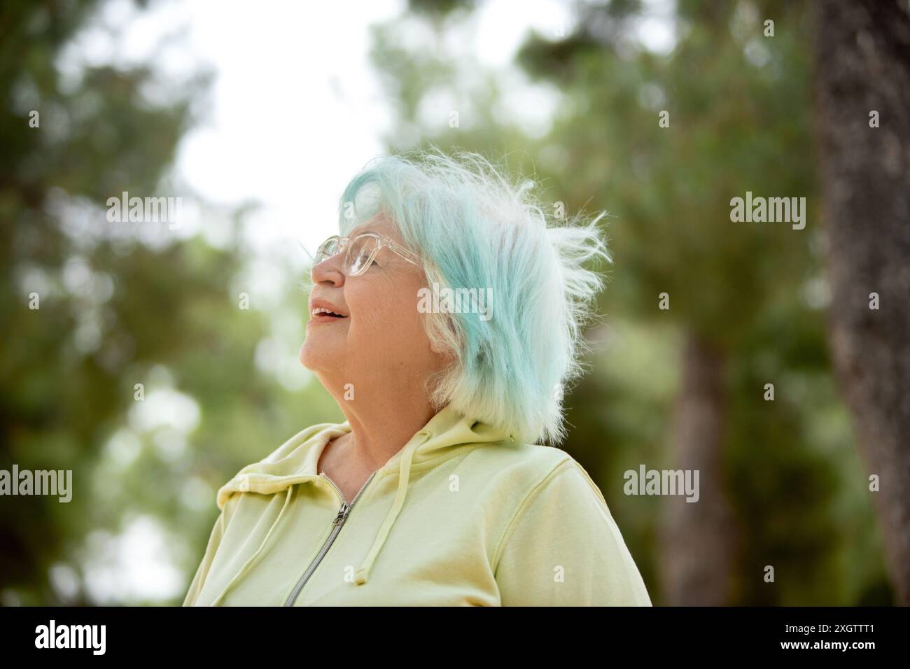 Una donna anziana guarda verso l'alto mentre si rilassa all'aperto, circondata da alberi. Foto Stock