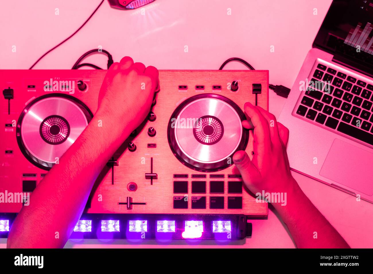 Il DJ regola i comandi di una console di mixaggio sotto intense luci rosa, riflettendo l'atmosfera di una festa o di un club e mostrando la tecnologia utilizzata in mi Foto Stock