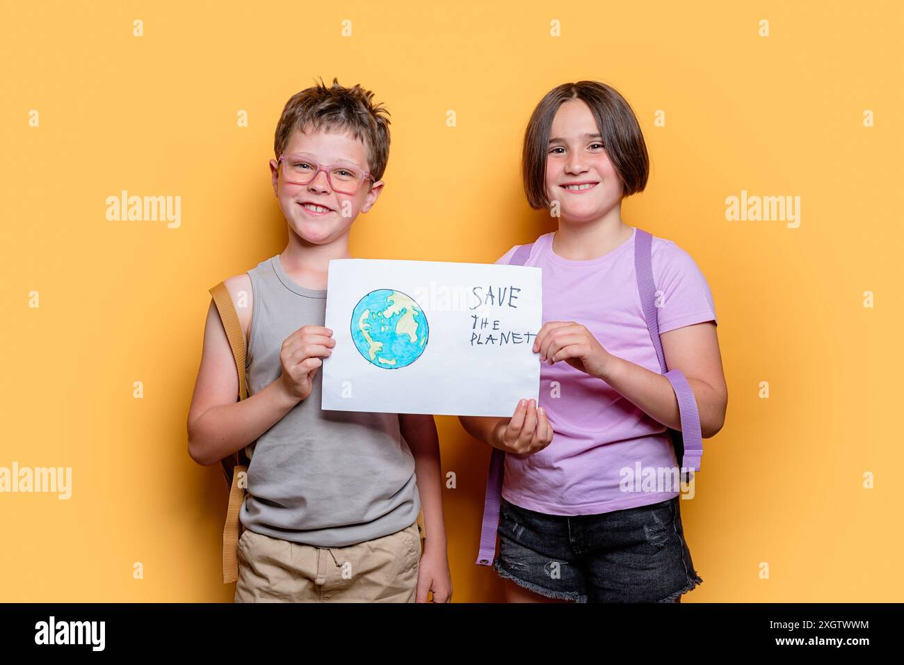 Sorridente ragazzo e ragazza in uno studio, con in mano un cartello con la scritta Save the Planet, ambientato su uno sfondo giallo brillante Foto Stock