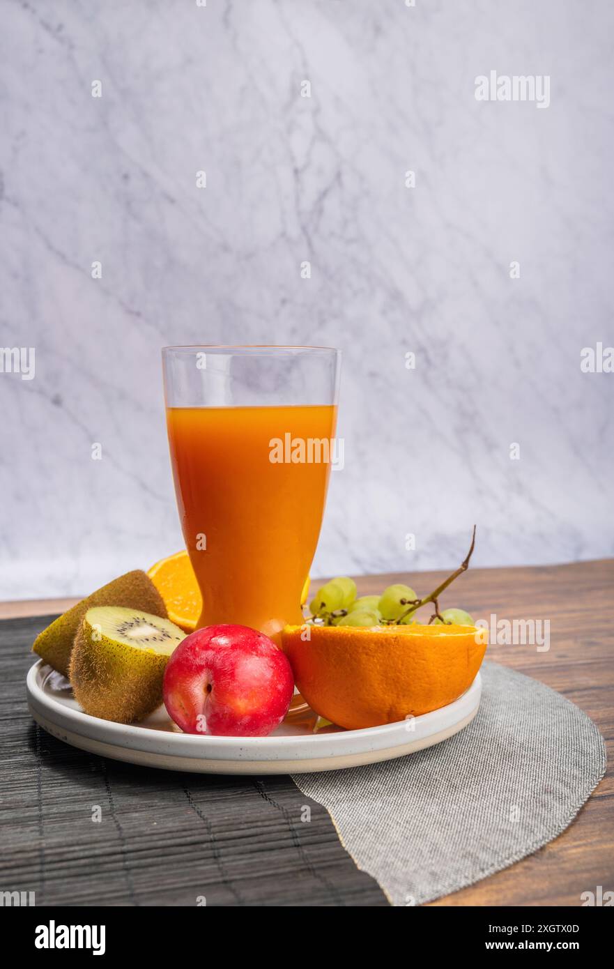 Vivace selezione di frutta fresca tra cui kiwi, arancia, mela e uva, insieme a un bicchiere di succo d'arancia. Tutti gli articoli sono ordinatamente disposti su un circ Foto Stock