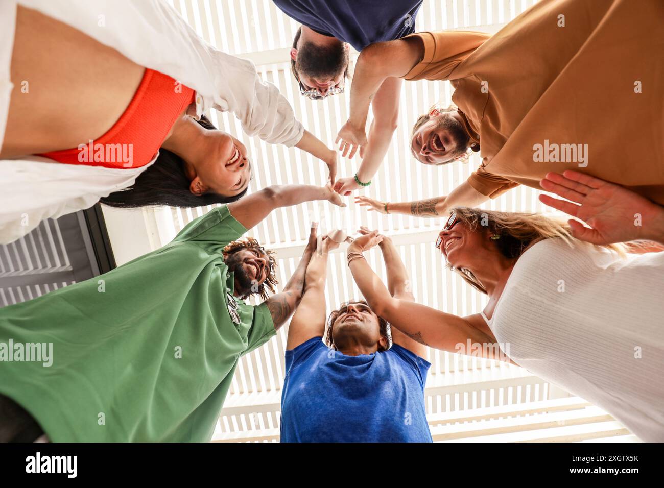 Un gruppo eterogeneo di amici che formano un cerchio e danno a un gruppo cinque alti, visti da un angolo basso su uno sfondo luminoso. Il gruppo include uomini Foto Stock