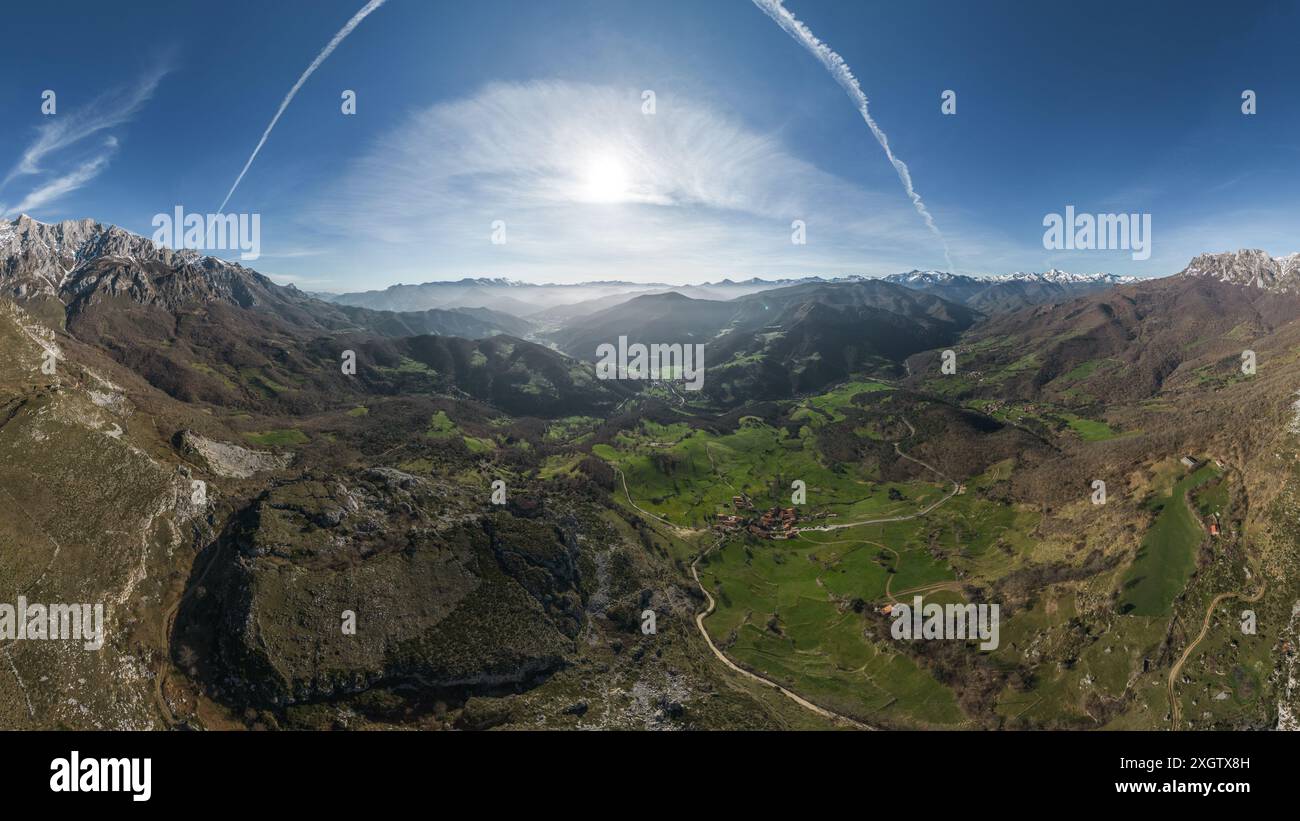 Paesaggio panoramico di lussureggianti vallate verdi circondate da torreggianti montagne con cime innevate sotto un cielo azzurro, attraversate da strade tortuose e. Foto Stock