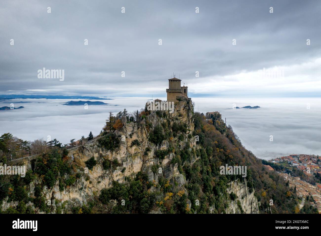 Vista aerea mozzafiato della prima torre Guaita in cima al castello di San Marino, arroccata su una scogliera circondata da un mare di nuvole e colline lontane Foto Stock