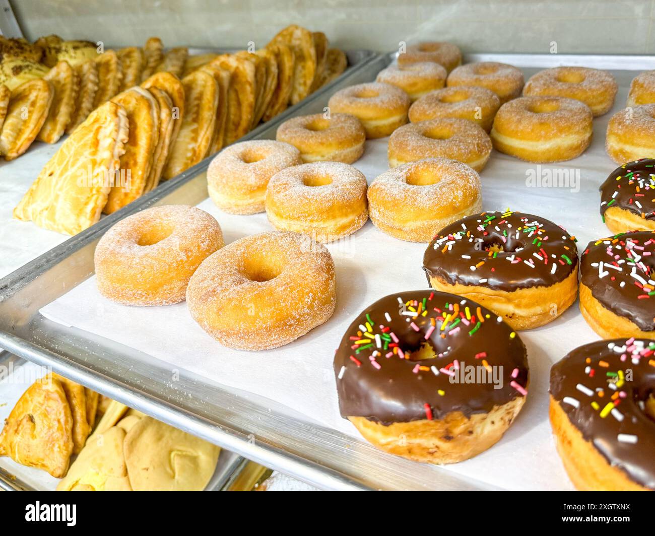 ciambelle assortite, tra cui varietà ricoperte di zucchero e smerigliate al cioccolato, insieme ad altri dolci Foto Stock