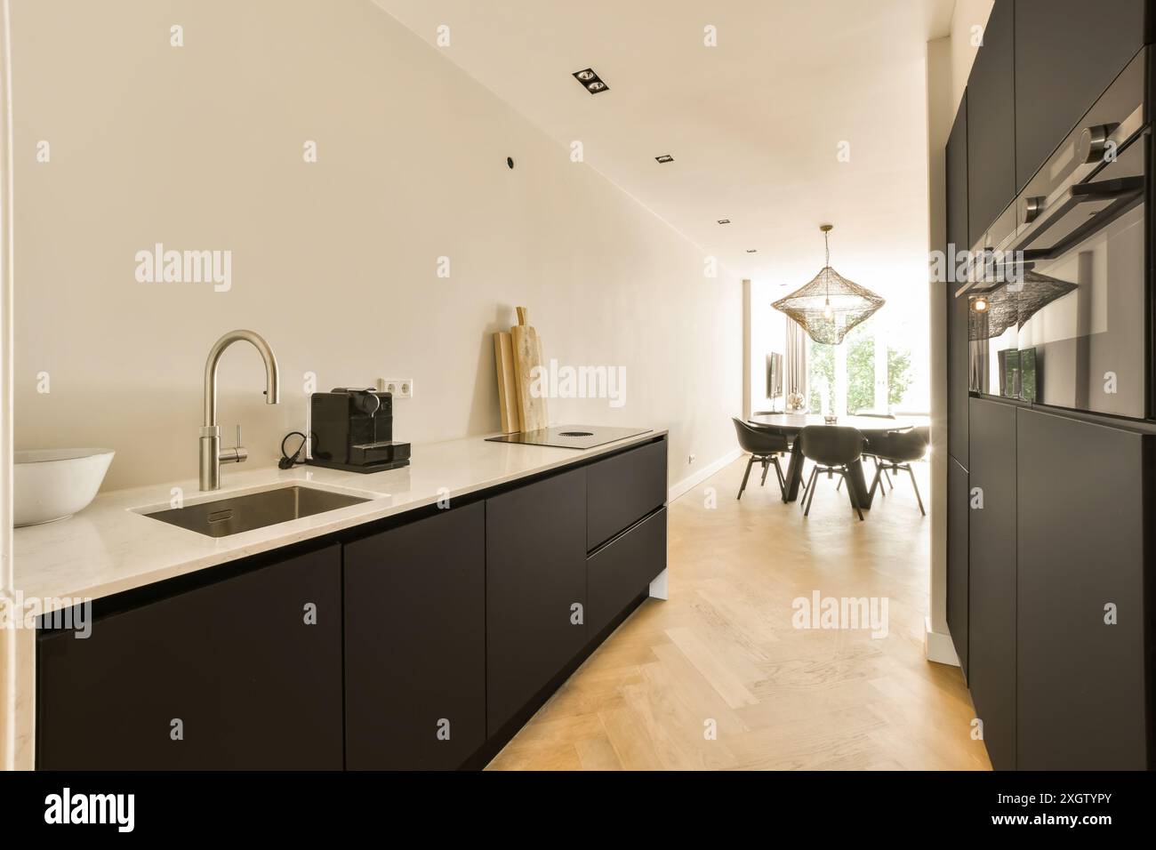 Una cucina spaziosa e ben illuminata con armadi neri e una zona pranzo con una lampada a sospensione unica. Foto Stock