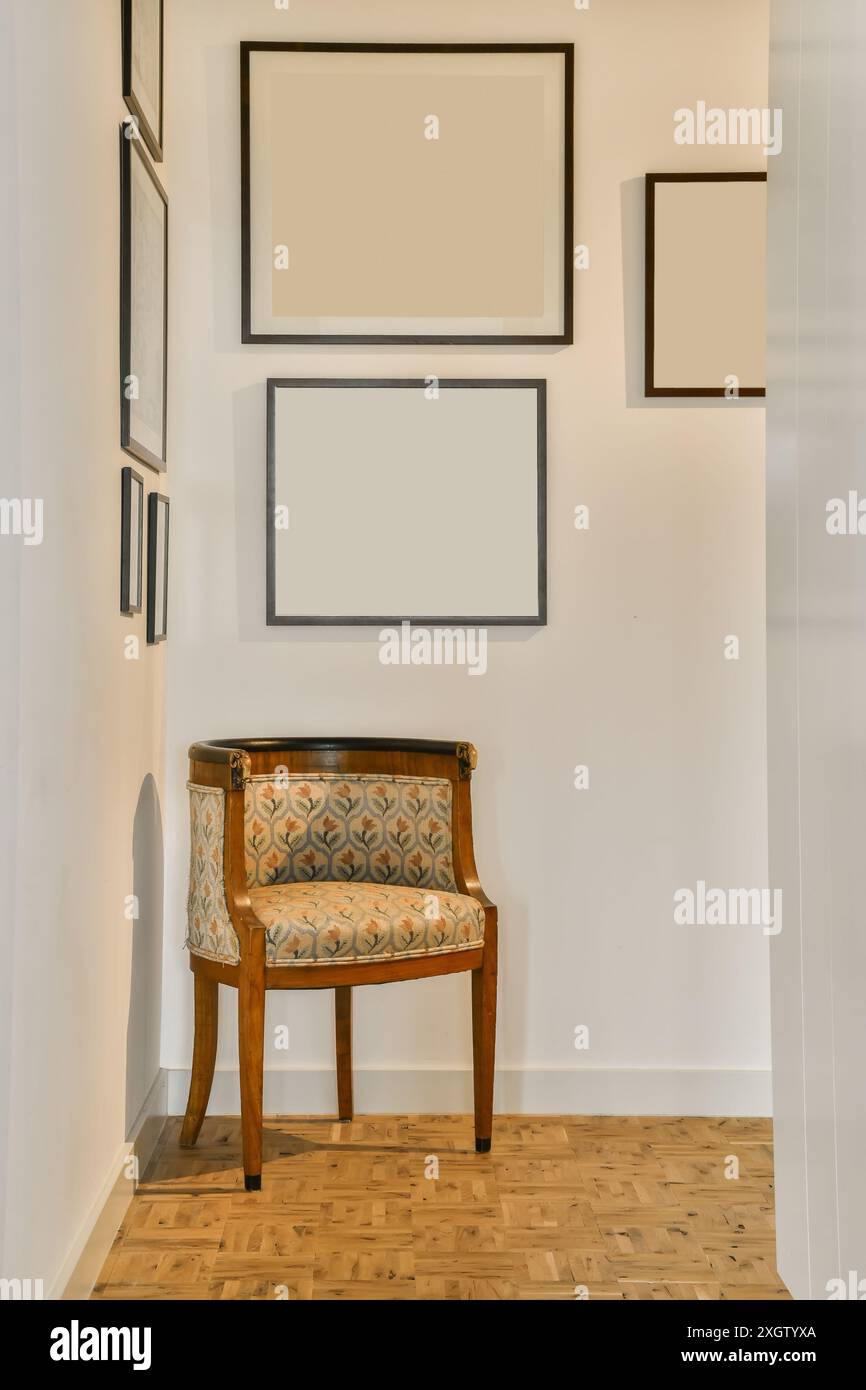Una sedia imbottita vintage si erge su una parete vuota adornata da cornici vuote in un ambiente di design moderno. Foto Stock