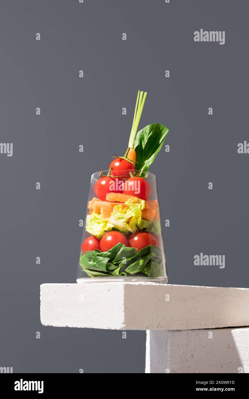 Insalata a strati fresca e colorata servita in vetro trasparente, elegantemente esposta su sfondo grigio. Opzione pasto salutare con una vasta gamma di ve Foto Stock