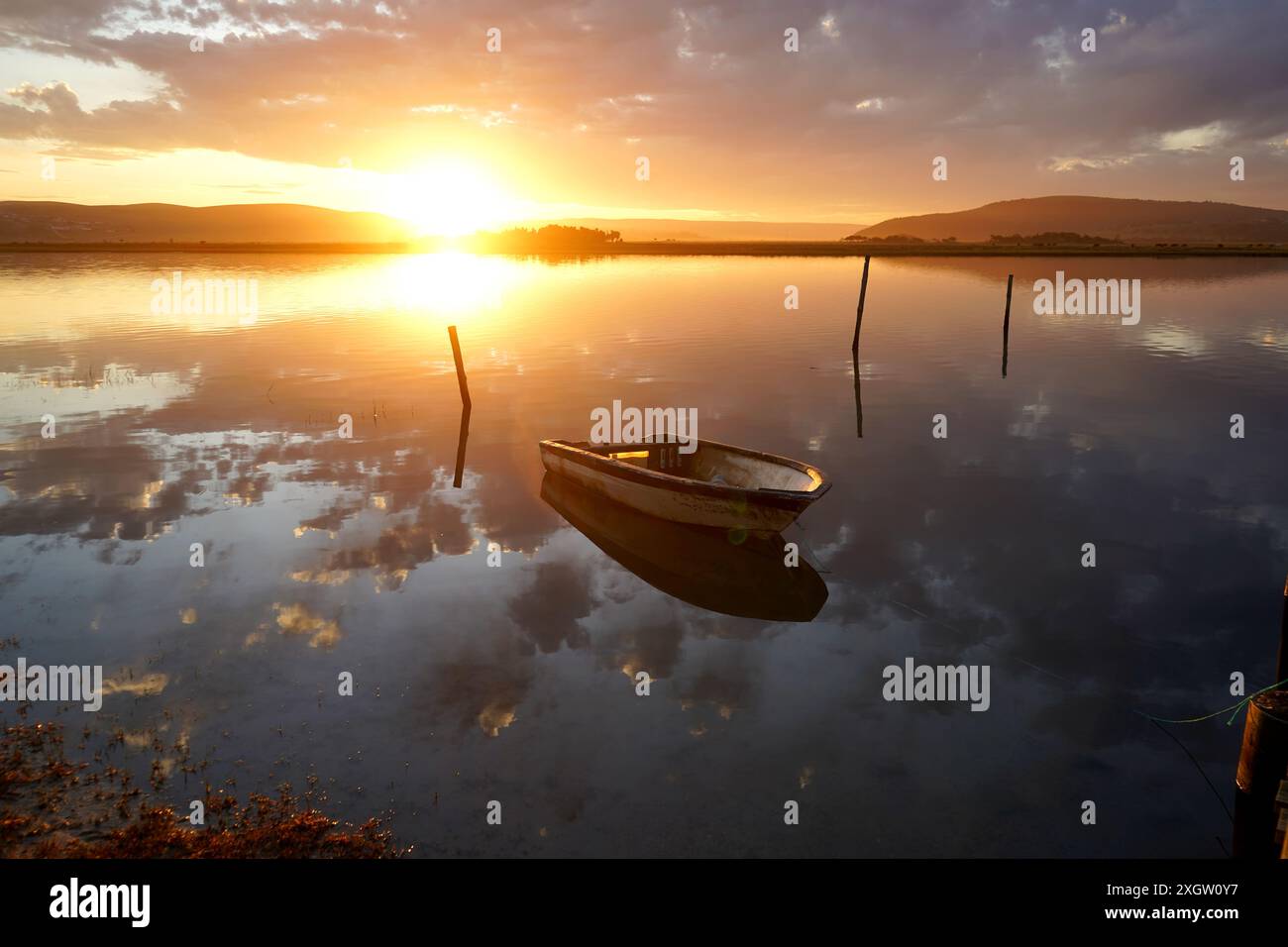 Vecchio molo in legno e perfetto riflesso della barca in un fiume al tramonto Foto Stock
