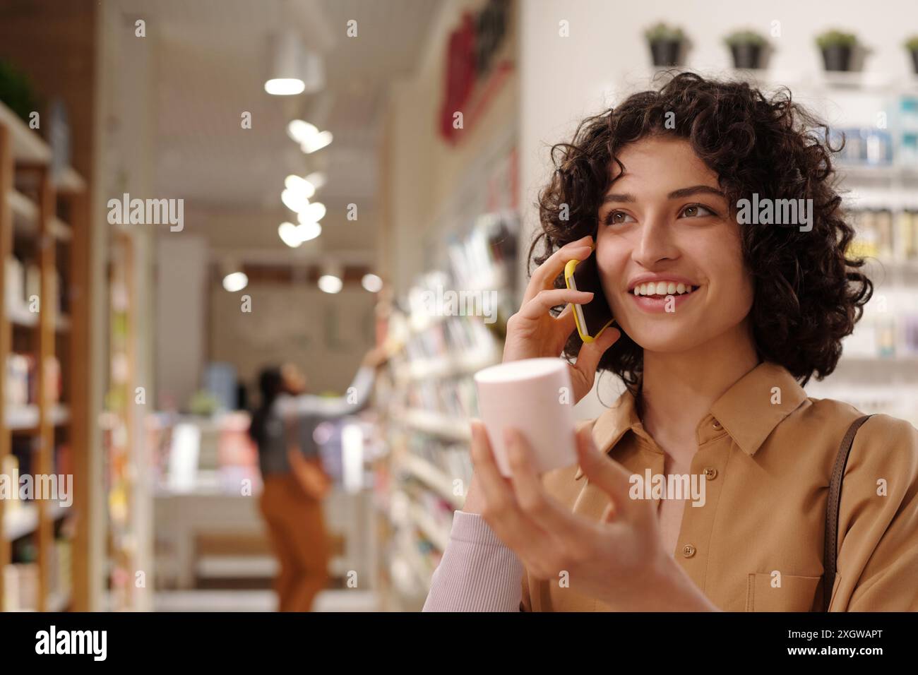 Una donna felice che fa acquisti con un telefono cellulare parlando con un'amica mentre la informa sulla nuova vendita stagionale nel supermercato cosmetico Foto Stock