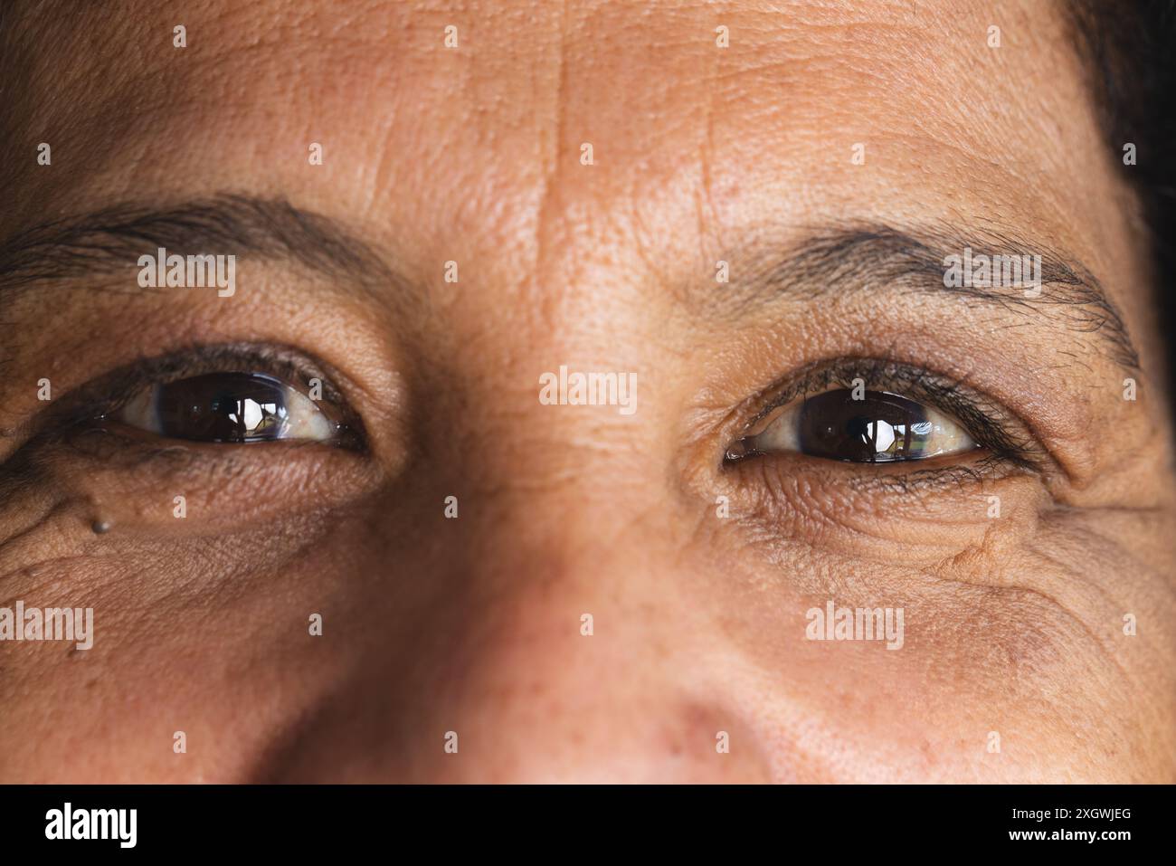 Ritratto primo piano di occhi marroni di una donna birazziale anziana felice sorridente a casa. Benessere, vita domestica e stile di vita per anziani, inalterati. Foto Stock