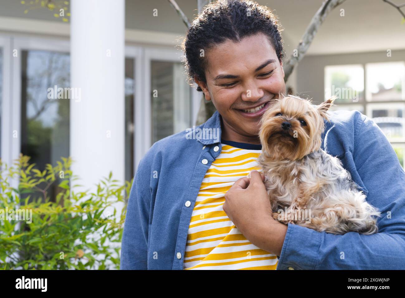 Il giovane uomo birazziale ama stare con il suo cane all'aperto, con spazio per copiare. Sorride in grande, mostrando un momento di gioia e compagnia in un ambiente domestico Foto Stock
