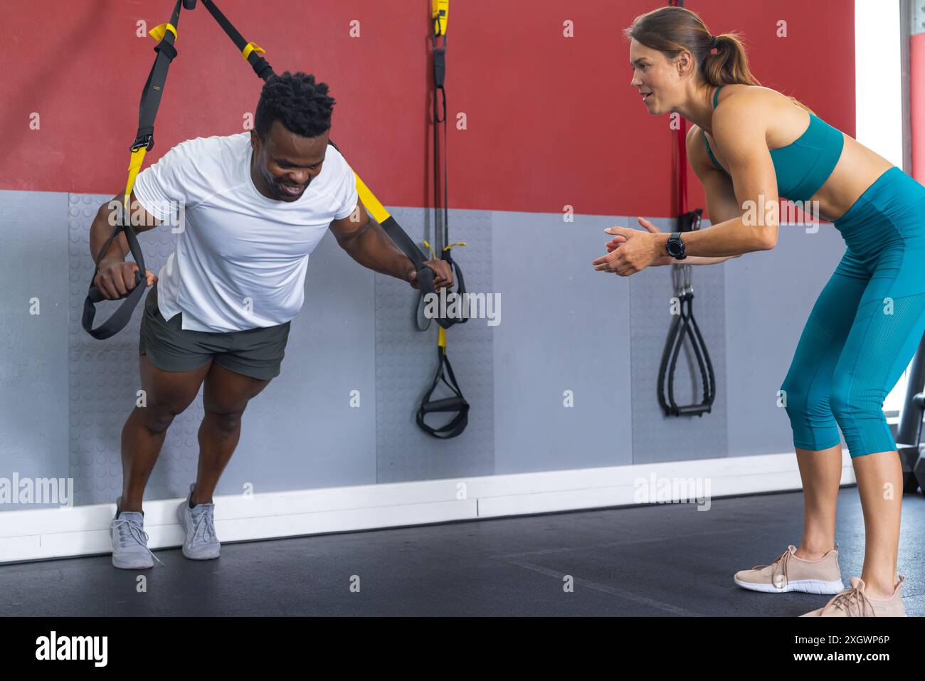Un uomo afro-americano si allena in palestra, con spazio fotocopie. È guidato da una giovane personal trainer caucasica. Foto Stock