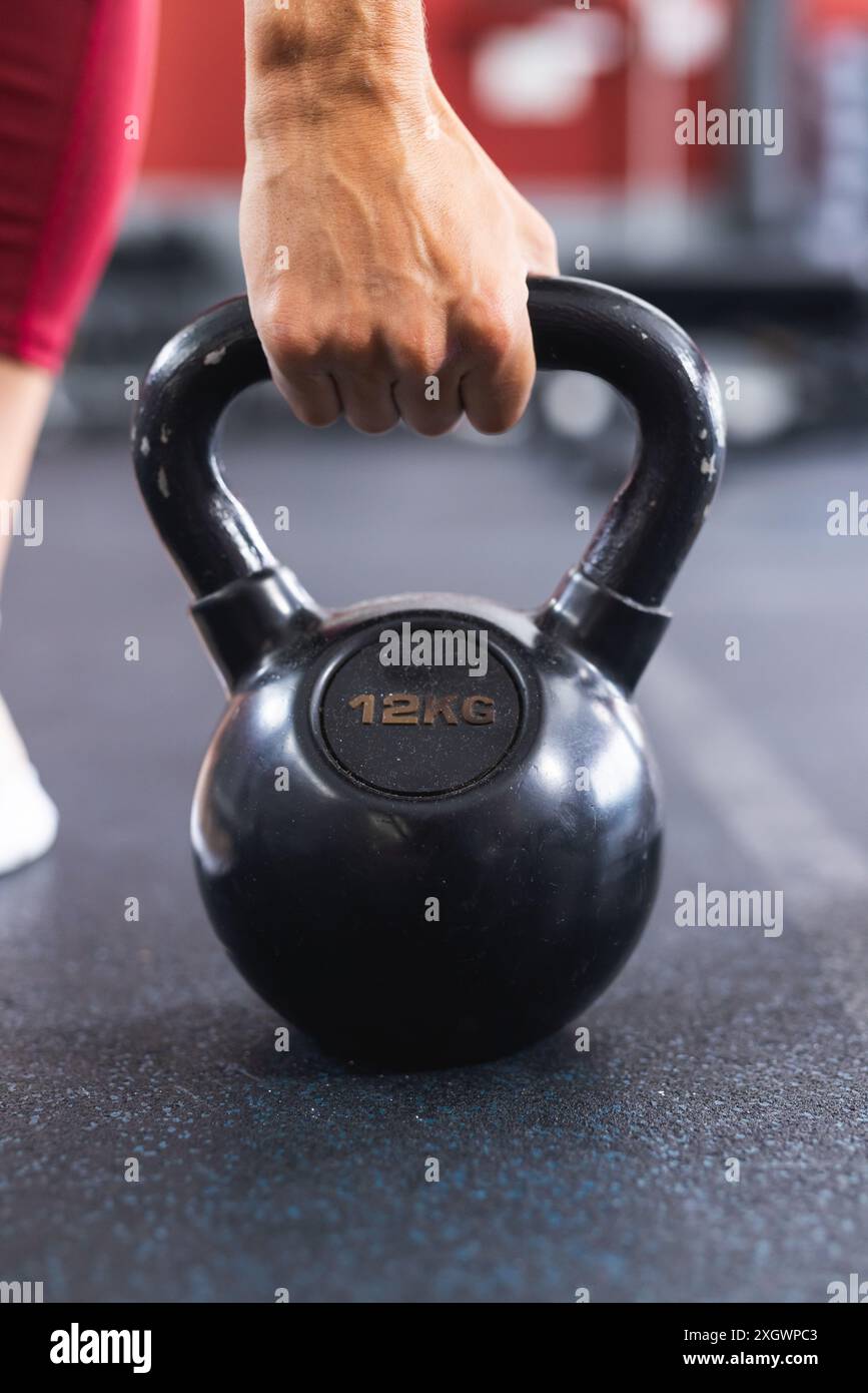 Primo piano di una mano in forma afferrando un campanello da 12 kg in palestra. Concentrandosi sull'allenamento di forza e sul fitness, l'immagine cattura un momento di allenamento. Foto Stock