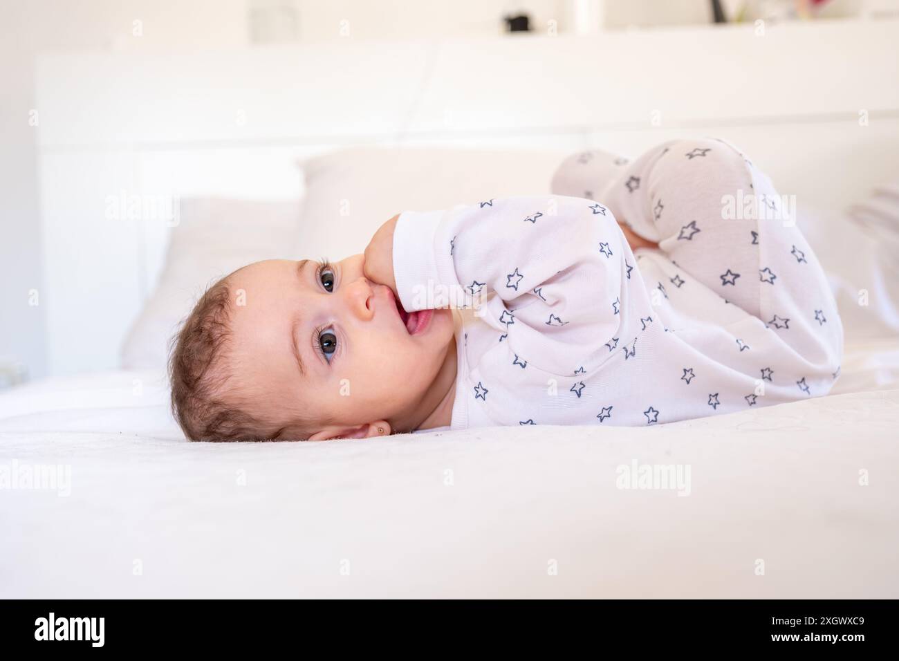 il bambino sorride allegramente su un lenzuolo bianco sul letto Foto Stock