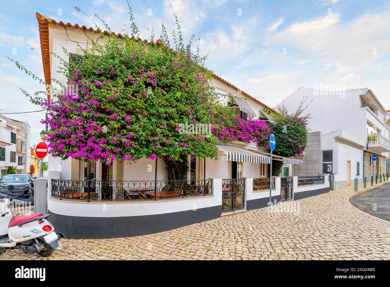 Un pittoresco caffè con posti a sedere all'aperto e piante di Bougainvillea in fiore viola nel centro storico di Cascais, in Portogallo. Foto Stock