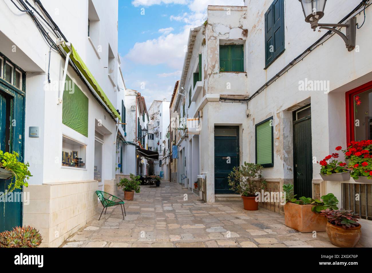 Una strada stretta con negozi e caffetterie sul marciapiede nello storico villaggio di Mahon, in Spagna, sull'isola mediterranea di Minorca. Foto Stock