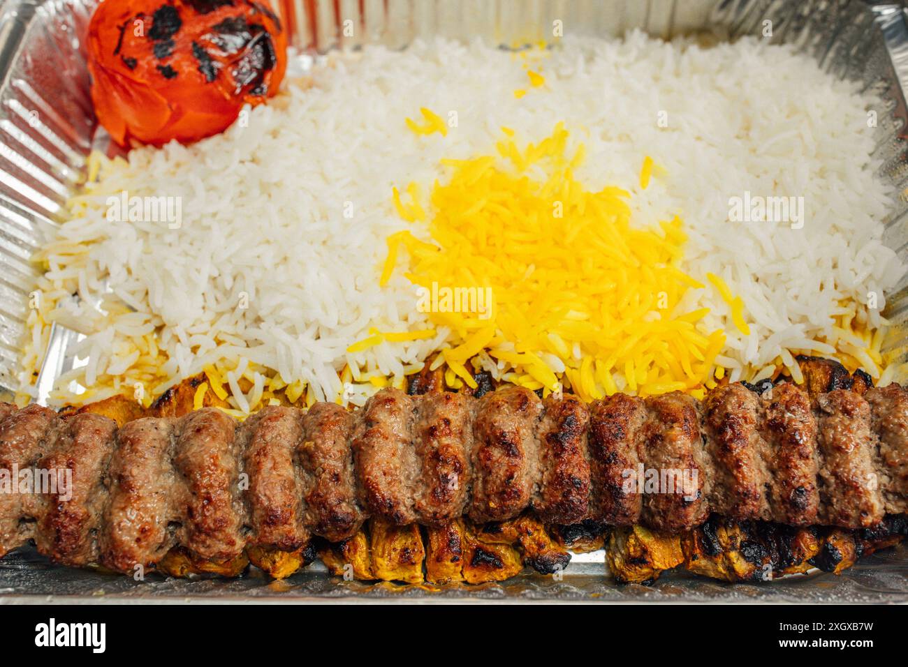 Piatto da asporto di cibo persiano: Riso basmati cosparso di riso allo zafferano, kabob koobideh, pomodoro intero grigliato Foto Stock