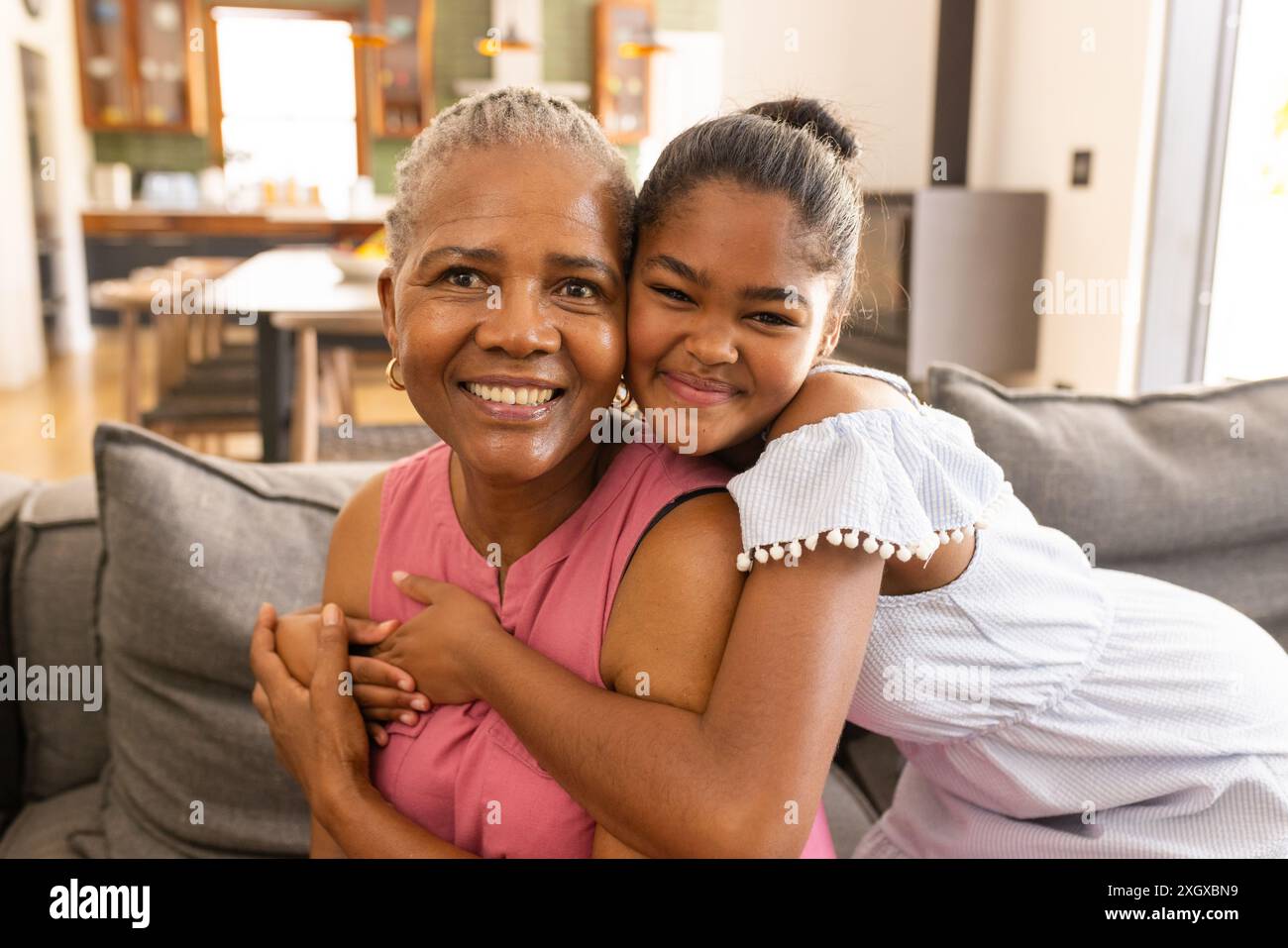 La nonna afroamericana senior abbraccia una nipote birazziale adolescente a casa. I loro sorrisi caldi riflettono un forte legame familiare, inalterato, in un Foto Stock