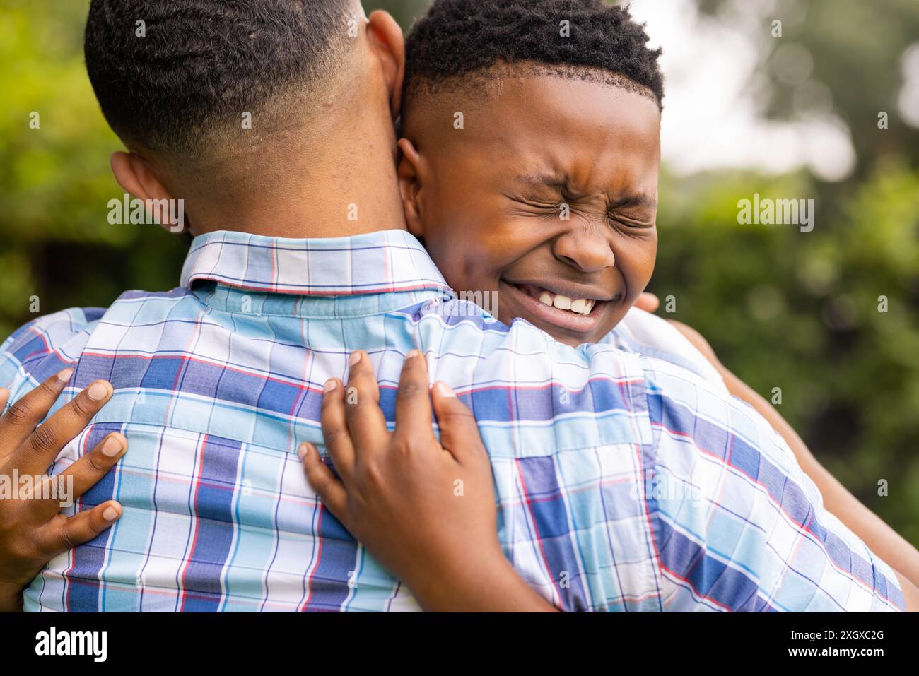 Il giovane padre afroamericano abbraccia suo figlio afroamericano all'aperto. Il loro caldo abbraccio trasmette un forte legame e un rapporto affettuoso. Foto Stock