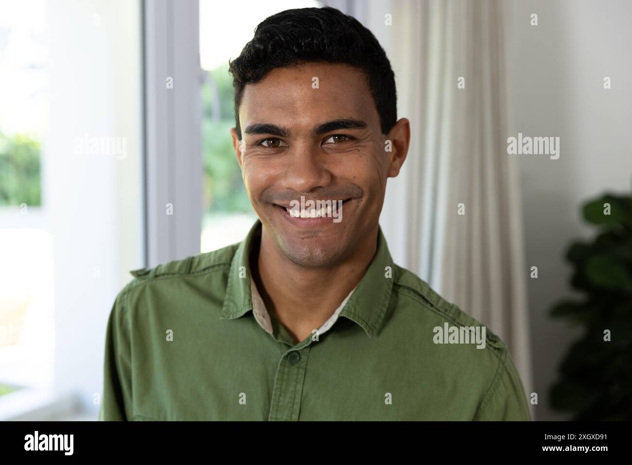 Il giovane uomo birazziale sorride calorosamente in un ambiente domestico. La sua espressione allegra aggiunge un'atmosfera accogliente agli interni accoglienti, inalterati. Foto Stock