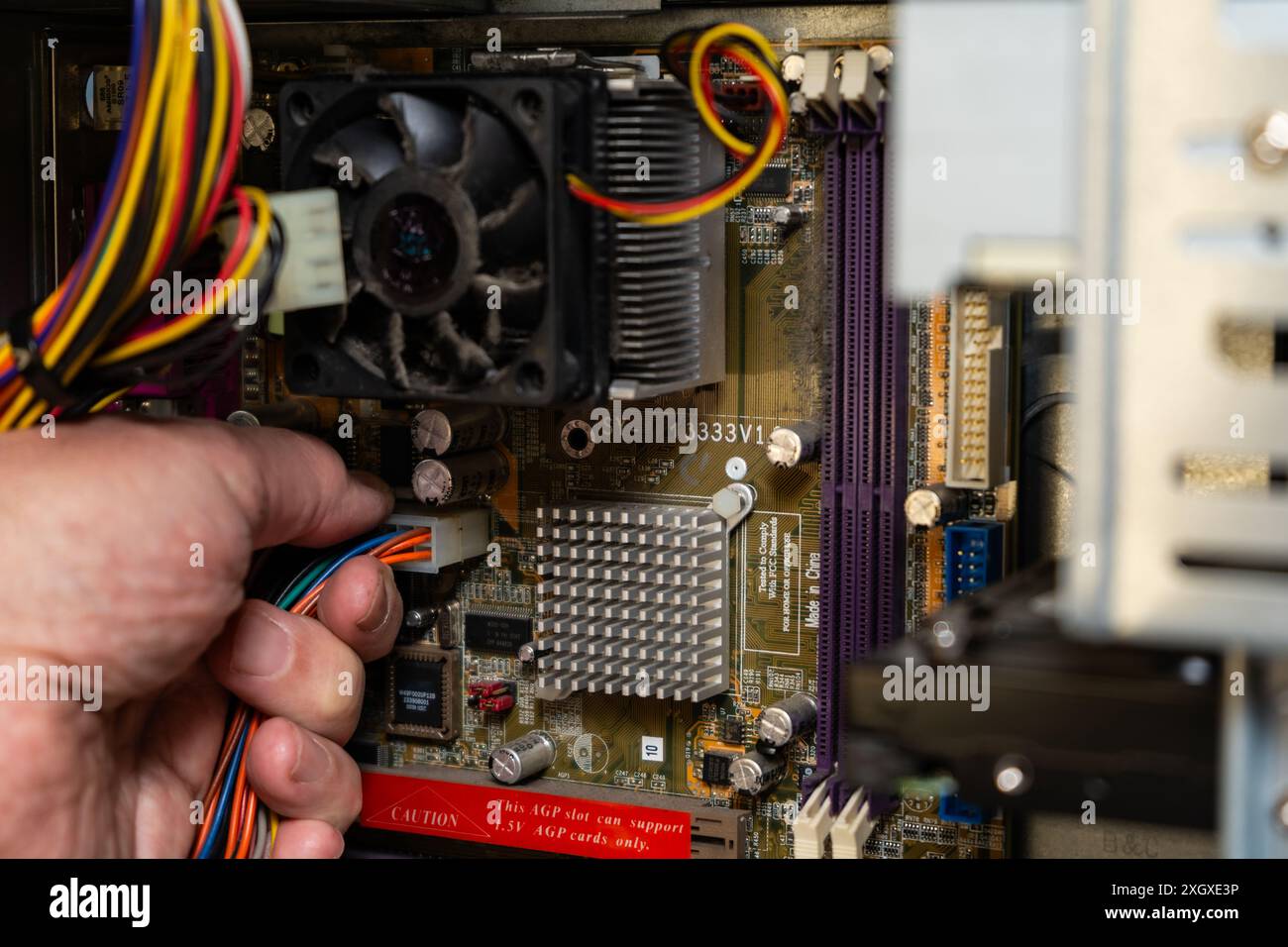 Mano di un tecnico che scollega l'alimentatore dalla scheda madre di un computer. Foto Stock