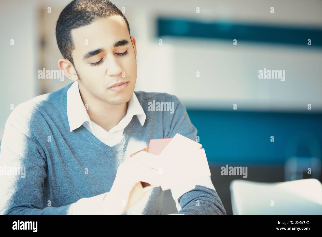 Un giovane uomo concentrato in una stanza ben illuminata contiene campioni di colore, considerando le opzioni disponibili. È vestito con un maglione grigio e una camicia bianca, con luce naturale Foto Stock