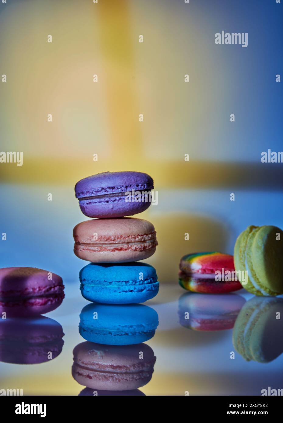 Un assortimento di macaron luminosi di diversi colori viene visualizzato su una superficie in vetro con uno sfondo decorativo astratto illuminato in pa diversi Foto Stock