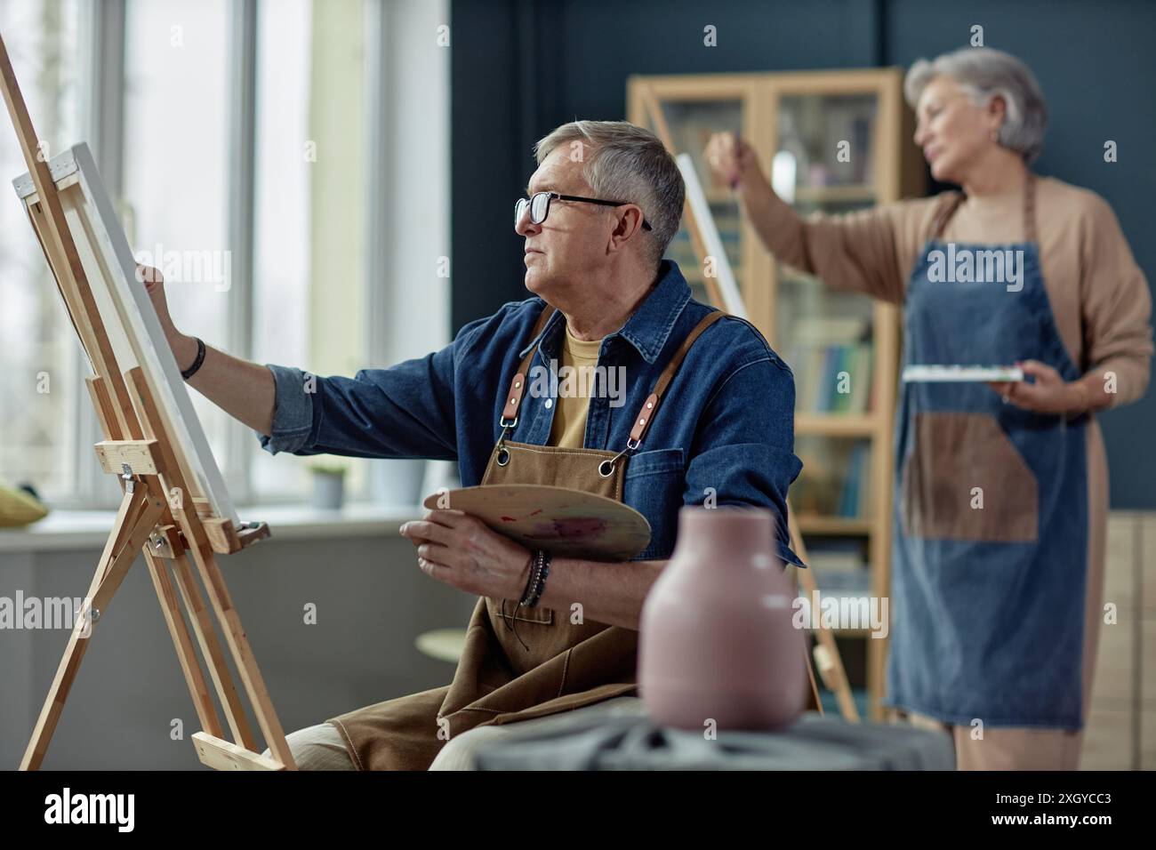 Vista laterale del ritratto di un anziano artista che dipinge su cavalletto in uno studio d'arte godendo di uno spazio di copia per hobby creativo Foto Stock