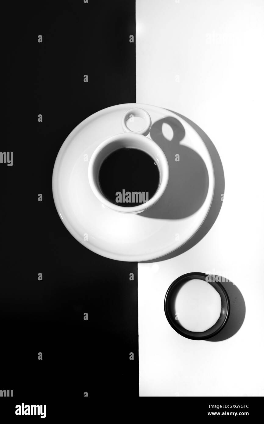 Tazza bianca con caffè nero e piccola ciotola nera di latte su sfondo minimalista bianco e nero Foto Stock