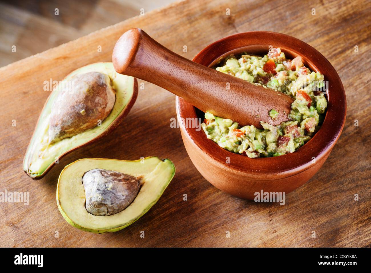 Vista ravvicinata degli avocado e guacamole fresco fatto in casa in mortaio di legno con pestello (molcajete). Salsa messicana tradizionale di avocado maturi. Foto Stock