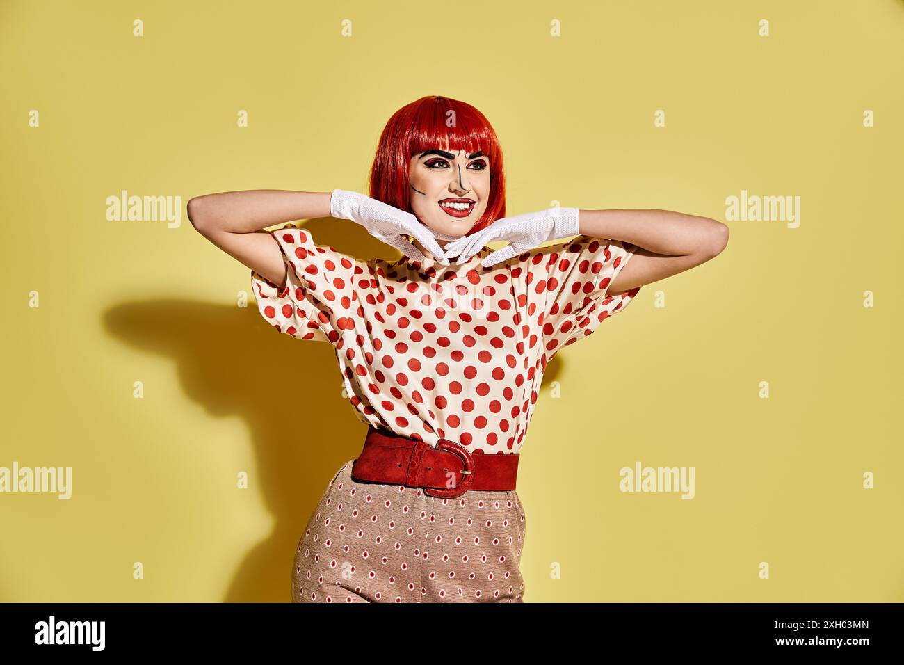 Vivace donna rossa con un creativo trucco pop art in una camicia a pois su sfondo giallo brillante, che trasuda l'atmosfera dei personaggi dei fumetti. Foto Stock