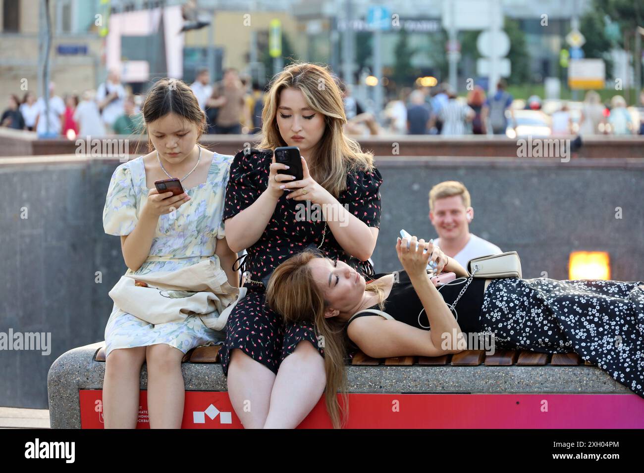 Ragazze asiatiche sedute con gli smartphone in strada. Utilizzo del telefono cellulare in città estiva Foto Stock