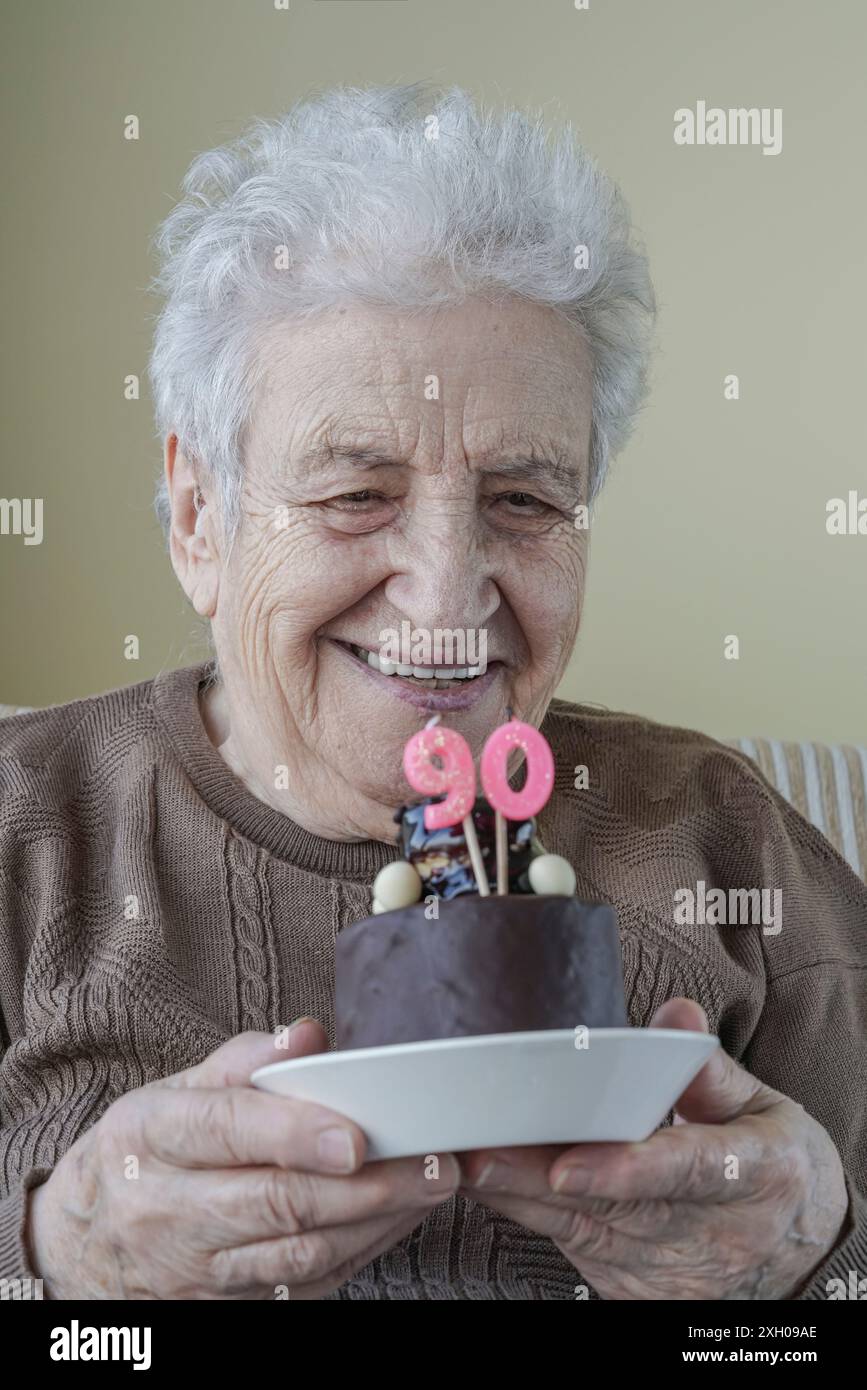 Una bella donna anziana che tiene la sua torta di compleanno per i novant'anni Foto Stock