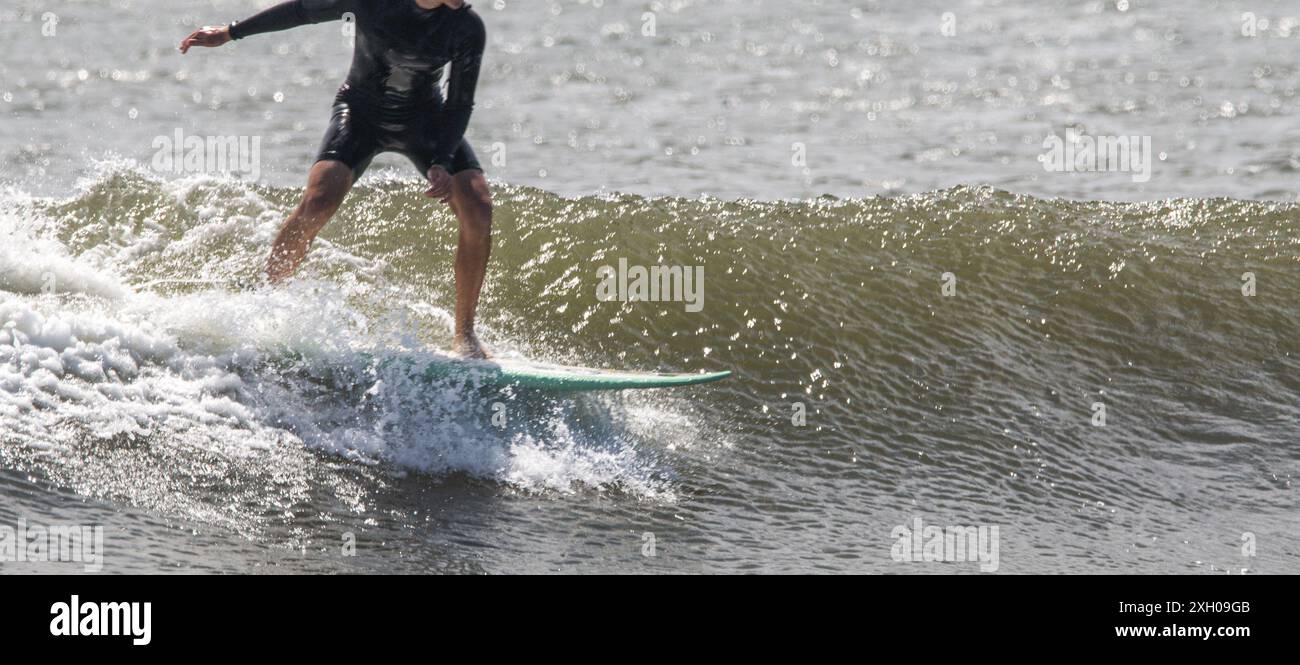 Vista laterale di un surfista in muta corta nera che cavalca un surf sulle onde della costa di Long Island Foto Stock