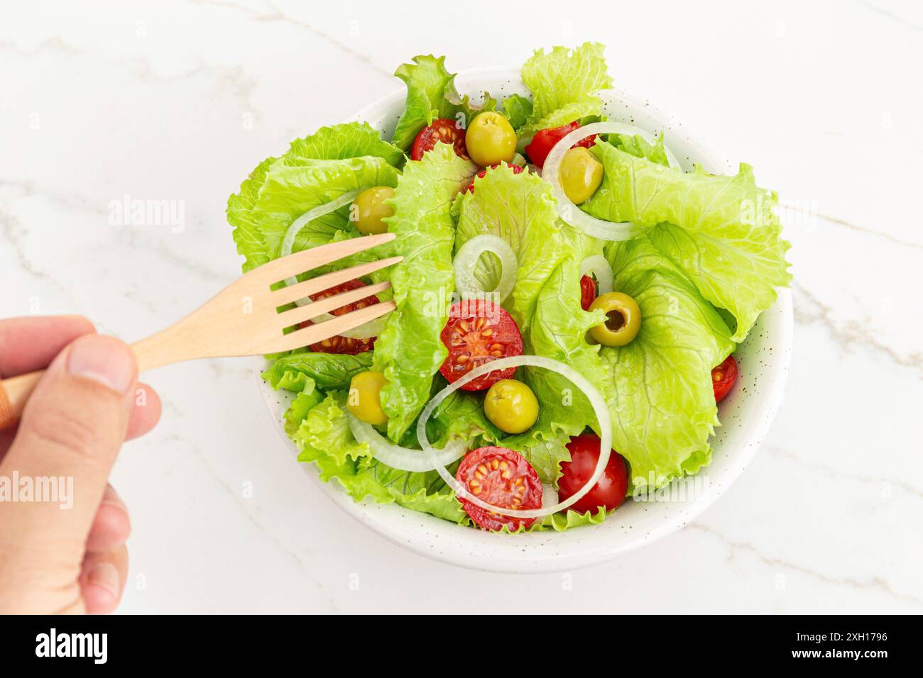 Mano di un uomo che mangia un'insalata fresca e sana in una ciotola. Cucina mediterranea Foto Stock