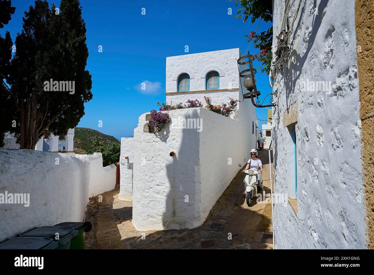 Vicolo stretto e soleggiato con edifici imbiancati, passa un autista di scooter, Chora, la città principale di Patmos, Patmos, la città vecchia, Dodecaneso, greco Foto Stock