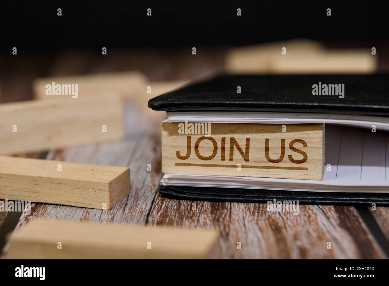 Blocchi di legno rustici scrivono "Unisciti a noi" su un blocco note, evocando un caloroso invito a collaborare e a connettersi. Foto Stock