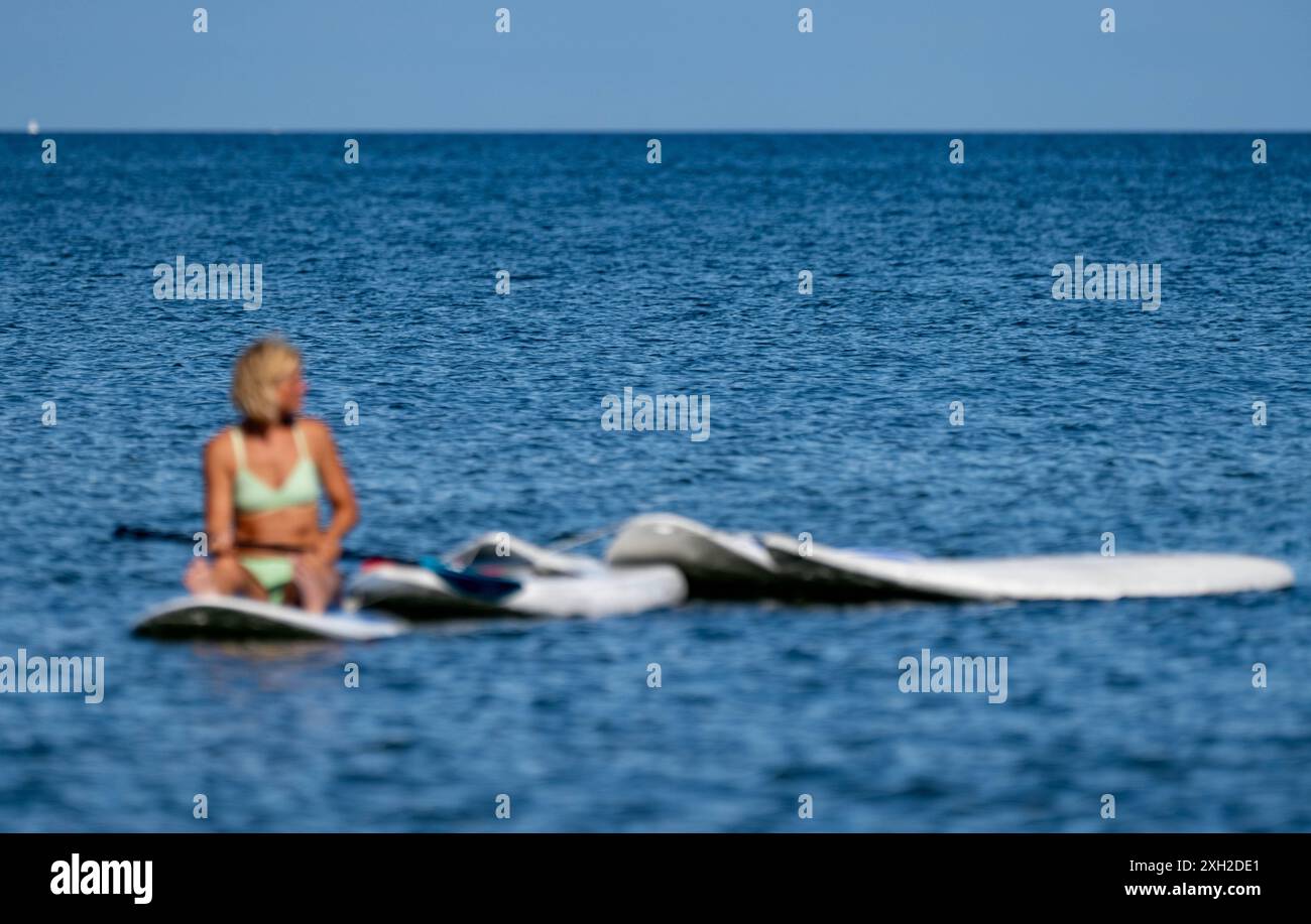 Prora, Germania. 11 luglio 2024. Maria, istruttore di surf, osserva gli studenti della scuola di vela Binz sul Mar Baltico al largo dell'isola di Rügen. Il più grande ostello della gioventù del Meclemburgo-Vorpommern a Prora ha aggiunto una scuola di surf alla sua gamma di servizi. La Binz Sailing School, fornitore della scuola di surf di Prora, offre ora corsi di windsurf e stand-up paddling, nonché tour guidati in kayak. Crediti: Stefan Sauer/dpa/ZB/dpa/Alamy Live News Foto Stock
