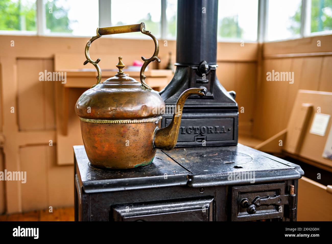 Bollitore vintage in rame su una classica stufa a legna in un ambiente accogliente e rustico. Foto Stock