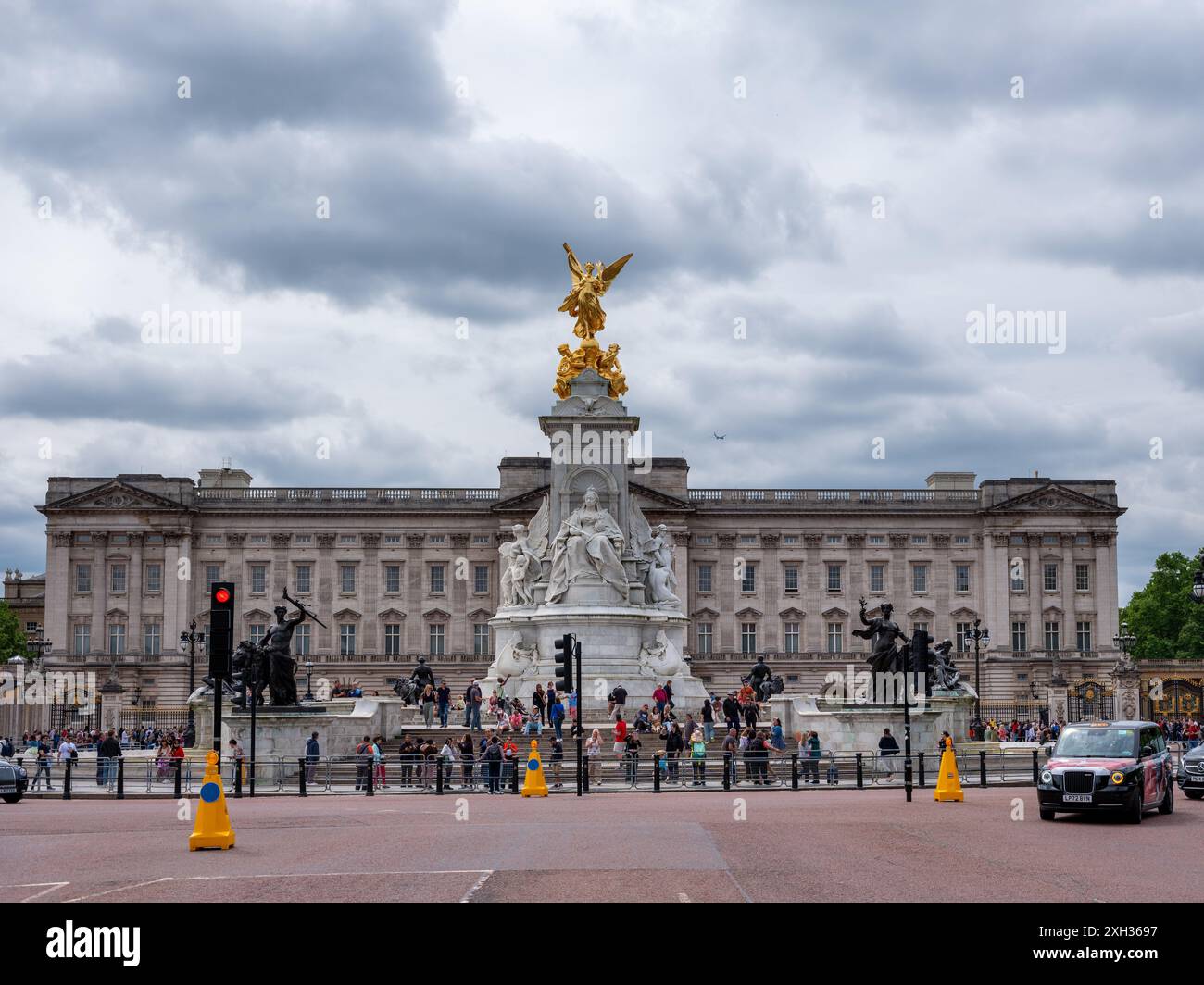 Londra, Inghilterra - 4 giugno 2024: Buckingham Palace con statua di Victoria e taxi nel traffico. Turisti visibili sulla strada. Foto Stock