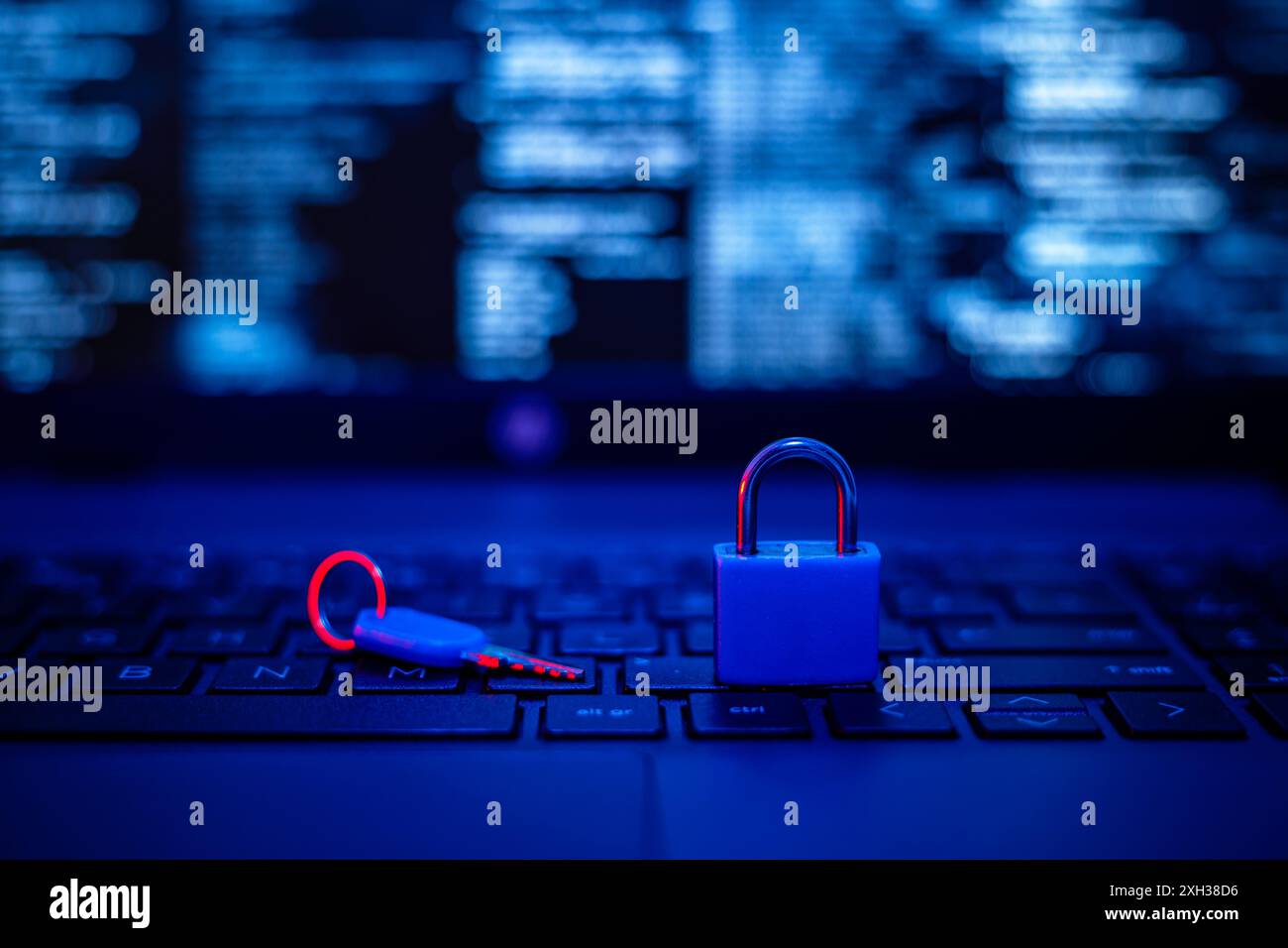 Un lucchetto blu si trova sulla tastiera di un notebook, con un tasto rosso accanto. La tastiera è illuminata in blu e viene visualizzata una schermata sfocata Foto Stock