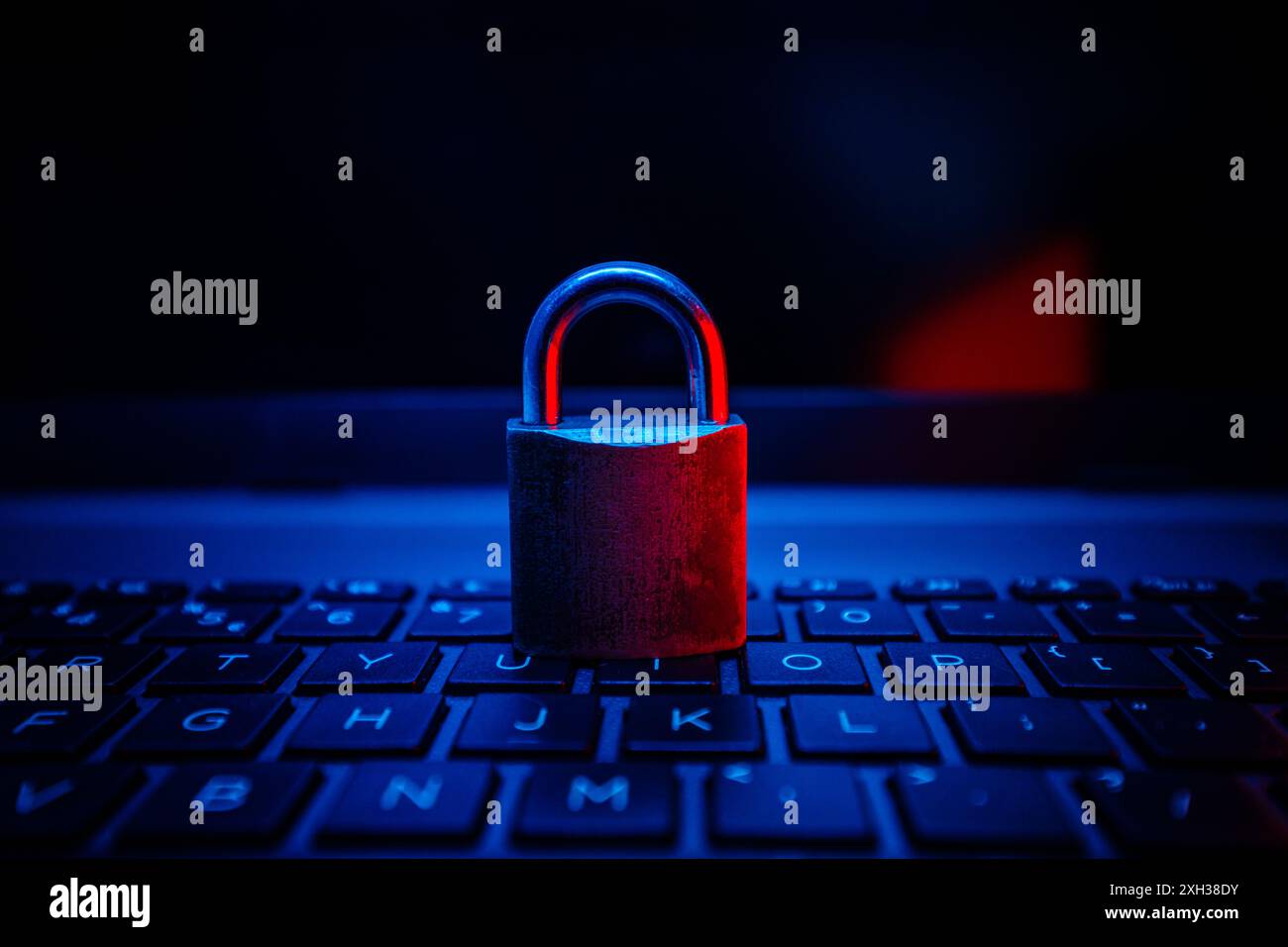 Un lucchetto metallico chiuso è posizionato sulla tastiera di un laptop illuminato da una luce blu e rossa. Foto Stock