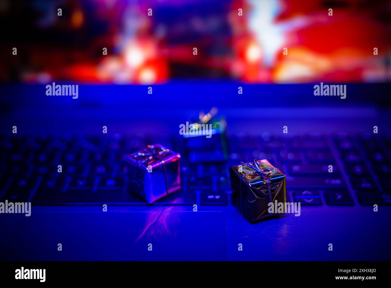 I piccoli regali si appoggiano sulla tastiera di un notebook con luci sfocate colorate sullo sfondo. Foto Stock