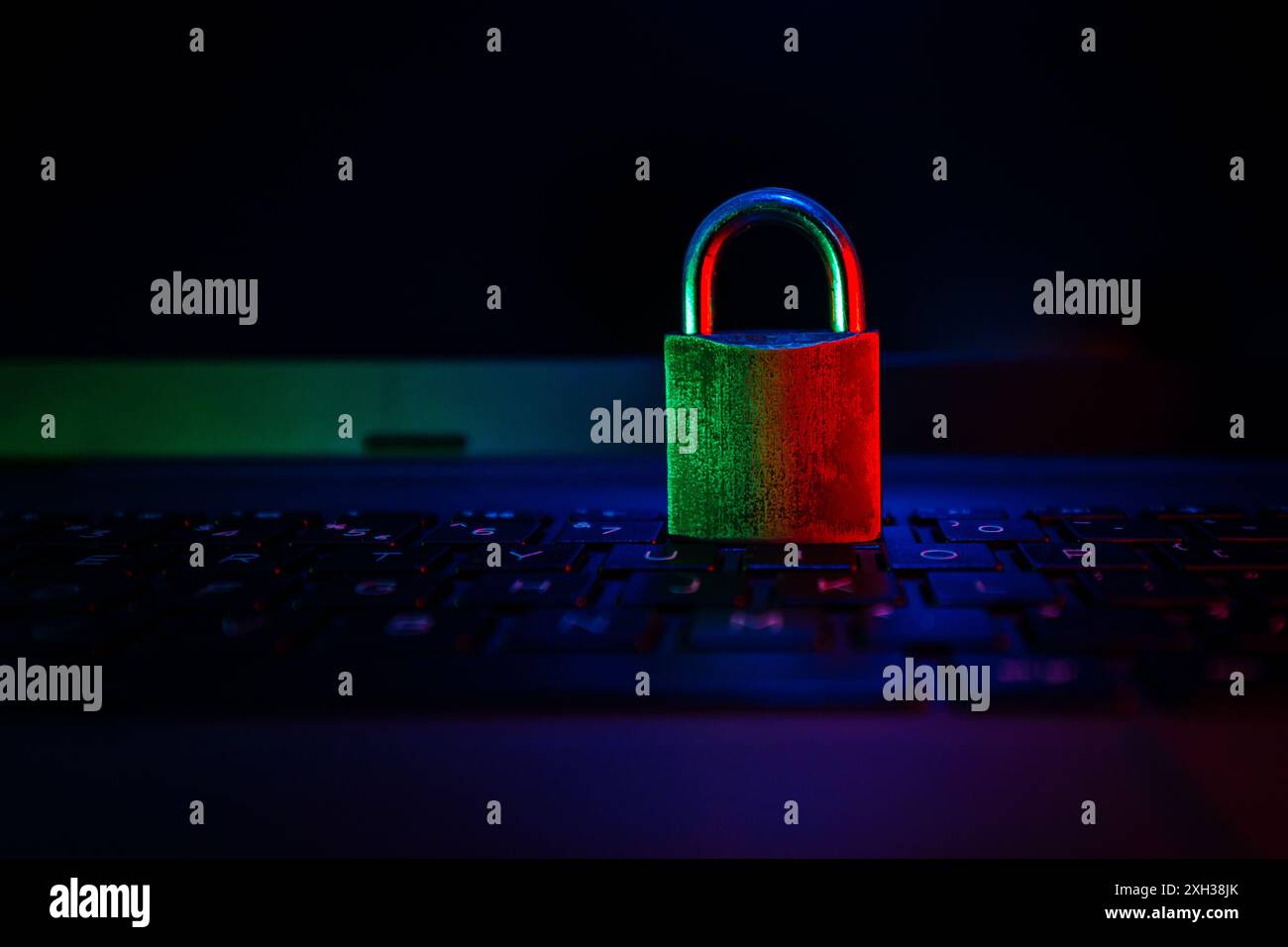 Un lucchetto verde e rosso si trova su una tastiera nera per laptop, illuminata da una luce blu morbida. Foto Stock