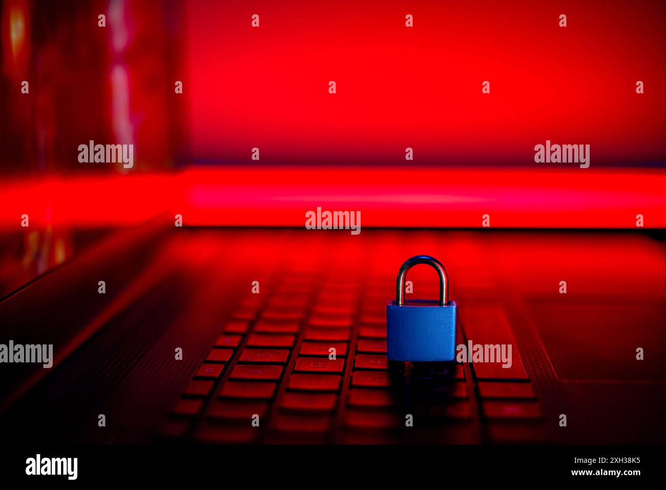 Un lucchetto blu poggia sulla tastiera di un notebook, con una luce rossa che illumina sullo sfondo. Foto Stock